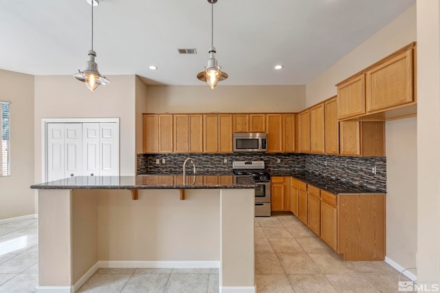 kitchen featuring a kitchen island with sink, appliances with stainless steel finishes, dark stone countertops, and pendant lighting