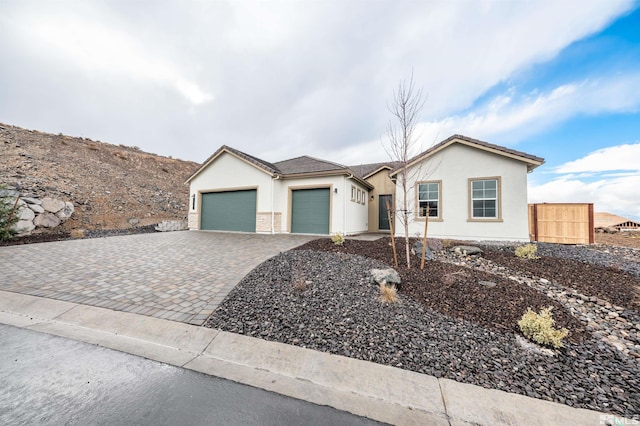 view of front of property with decorative driveway, fence, a garage, and stucco siding