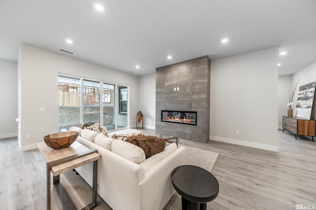 living room with recessed lighting, light wood-style flooring, a tile fireplace, and baseboards