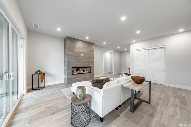 living area with visible vents, recessed lighting, a tile fireplace, and light wood-style floors