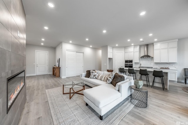 living area with a tiled fireplace, recessed lighting, light wood-style floors, and baseboards