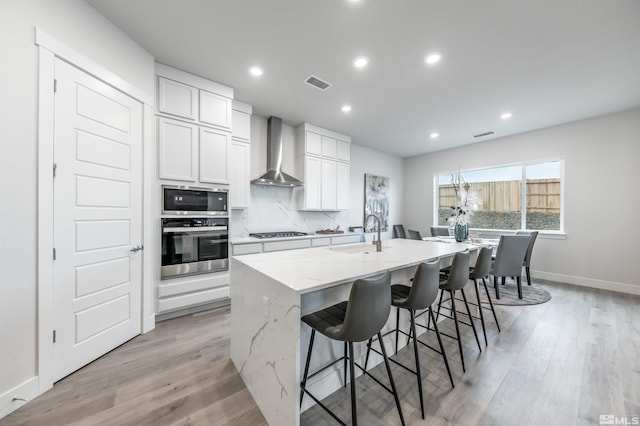 kitchen featuring visible vents, a kitchen island with sink, a sink, stainless steel appliances, and wall chimney exhaust hood