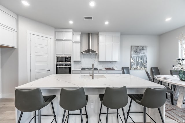 kitchen with light stone countertops, visible vents, stainless steel appliances, wall chimney exhaust hood, and backsplash