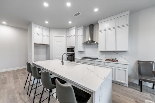 kitchen featuring visible vents, black appliances, light stone counters, backsplash, and wall chimney exhaust hood