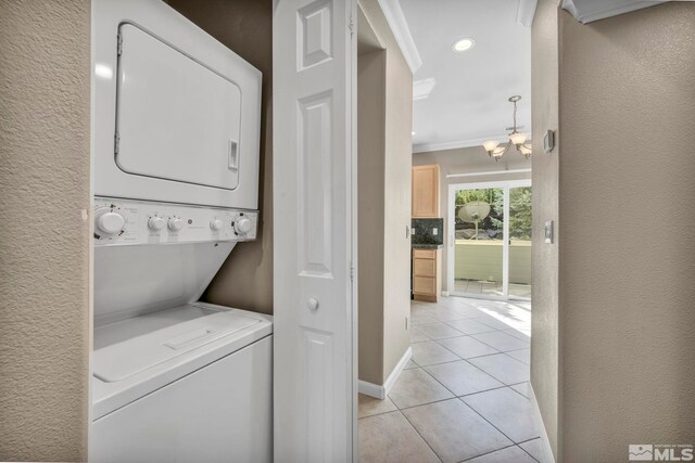 washroom with crown molding, a chandelier, light tile patterned floors, and stacked washer and dryer