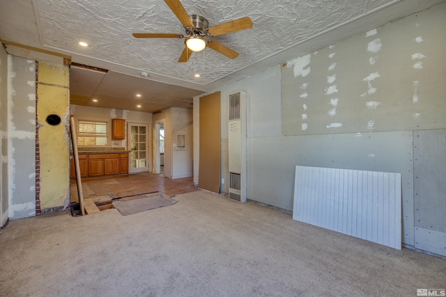 unfurnished living room with a textured ceiling, ceiling fan, and light carpet