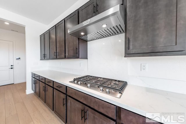 kitchen featuring light hardwood / wood-style floors, light stone counters, stainless steel gas cooktop, exhaust hood, and dark brown cabinets