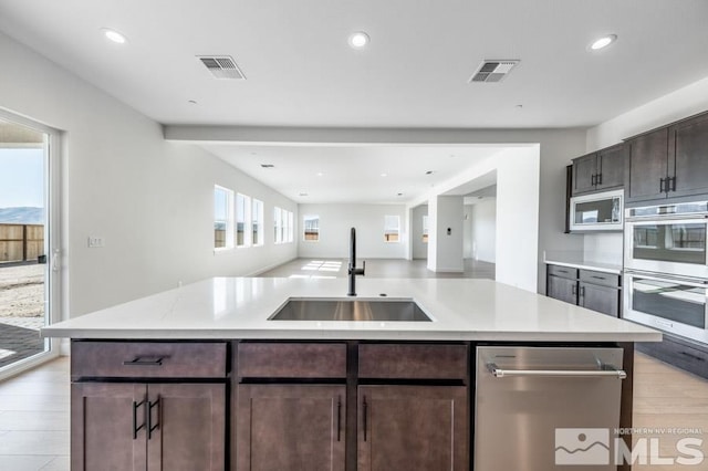 kitchen featuring dark brown cabinets, a kitchen island with sink, sink, light hardwood / wood-style flooring, and stainless steel appliances