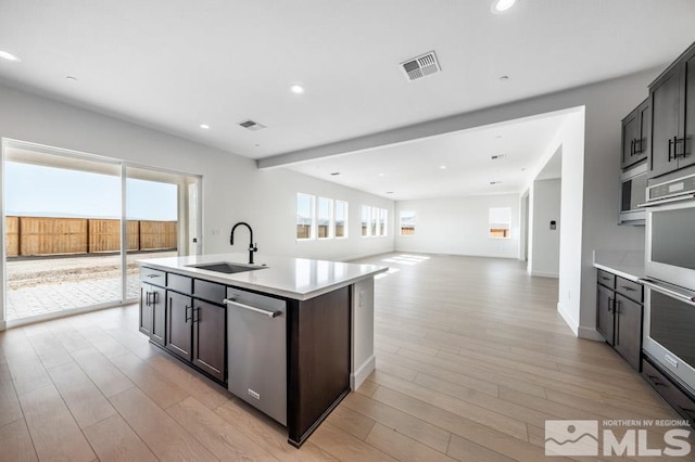 kitchen with appliances with stainless steel finishes, a center island with sink, light hardwood / wood-style floors, and sink