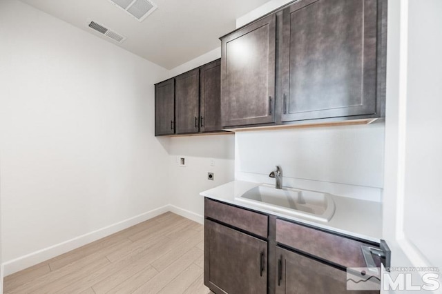 clothes washing area with light hardwood / wood-style floors, sink, electric dryer hookup, and cabinets