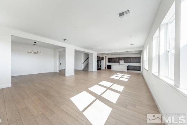 unfurnished living room with an inviting chandelier and light hardwood / wood-style flooring