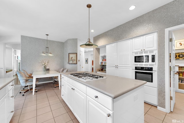 kitchen featuring white cabinets, decorative light fixtures, gas cooktop, stainless steel oven, and a kitchen island