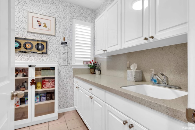 kitchen featuring sink, light tile patterned floors, white cabinetry, and light stone countertops