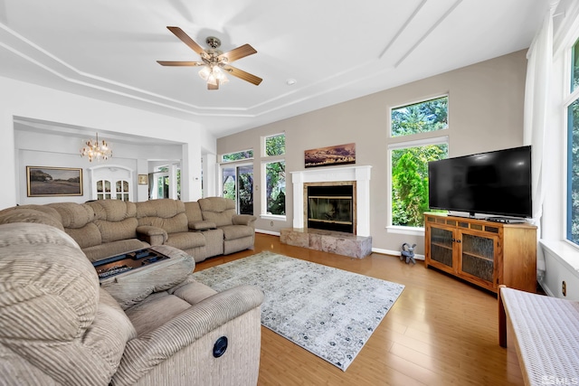 living room with a wealth of natural light, light hardwood / wood-style flooring, a high end fireplace, and ceiling fan with notable chandelier