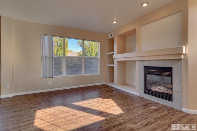 unfurnished living room with a tiled fireplace, dark hardwood / wood-style flooring, and built in shelves