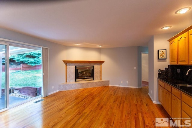 kitchen featuring backsplash, a fireplace, light wood-type flooring, and sink