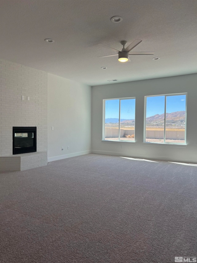 unfurnished living room featuring a textured ceiling, a brick fireplace, ceiling fan, and carpet