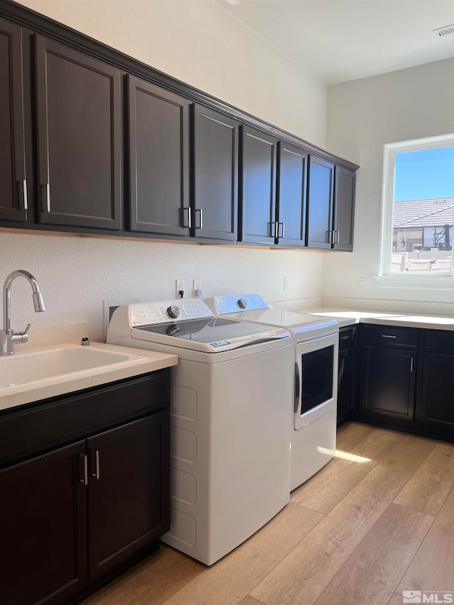 laundry area featuring washing machine and clothes dryer, cabinets, sink, and light hardwood / wood-style floors