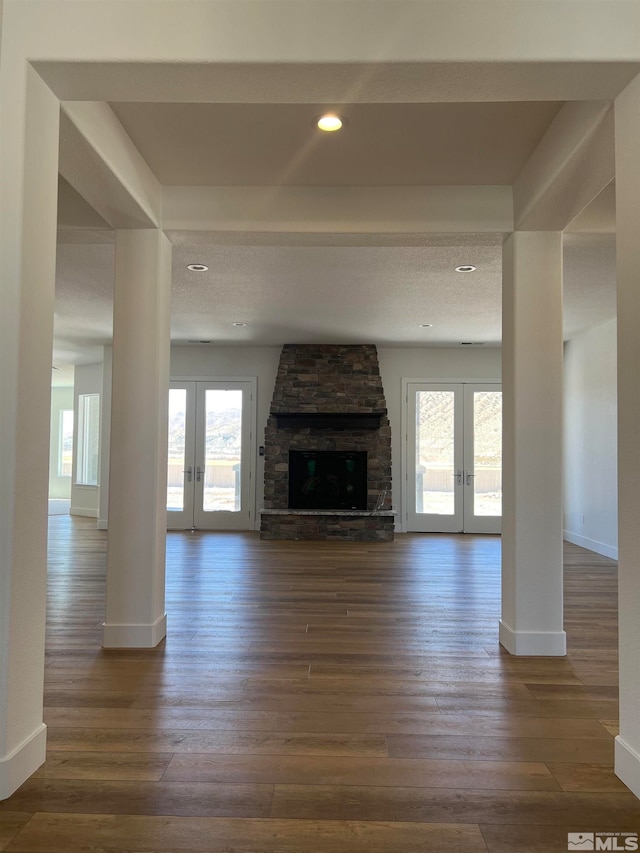 unfurnished living room with a textured ceiling, dark wood-type flooring, a stone fireplace, and french doors