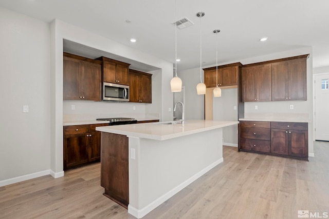 kitchen featuring sink, light wood-type flooring, decorative light fixtures, and an island with sink