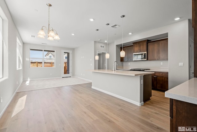 kitchen featuring light hardwood / wood-style floors, a notable chandelier, a center island with sink, and hanging light fixtures