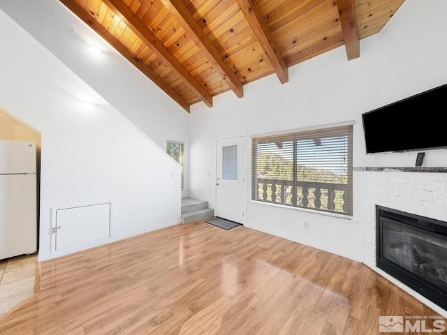 unfurnished living room with wood ceiling, beamed ceiling, light hardwood / wood-style flooring, and a stone fireplace