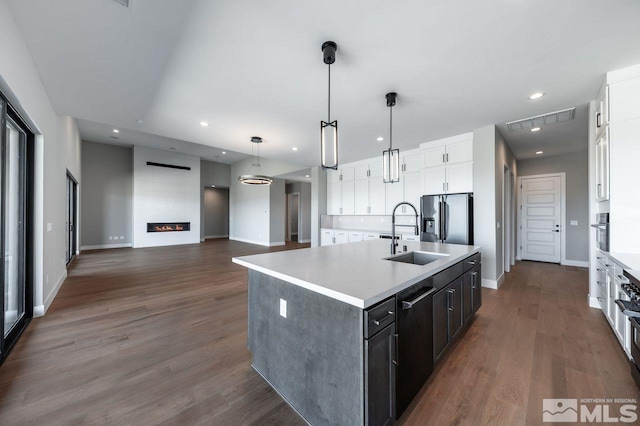 kitchen featuring a kitchen island with sink, sink, hanging light fixtures, appliances with stainless steel finishes, and white cabinets