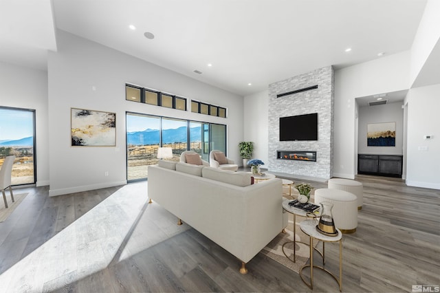 living room featuring wood-type flooring, a stone fireplace, and a towering ceiling