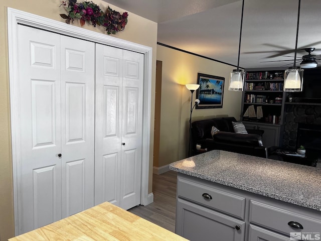 kitchen with gray cabinets, pendant lighting, ceiling fan, a stone fireplace, and dark hardwood / wood-style floors