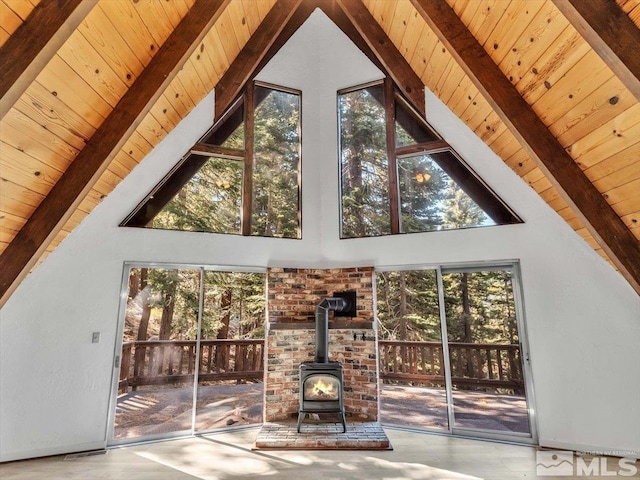 unfurnished living room featuring a wood stove, a healthy amount of sunlight, and beamed ceiling