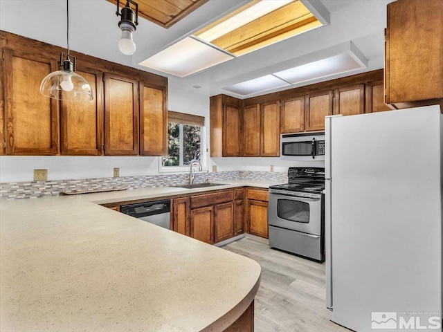 kitchen featuring decorative light fixtures, light hardwood / wood-style floors, stainless steel appliances, sink, and kitchen peninsula