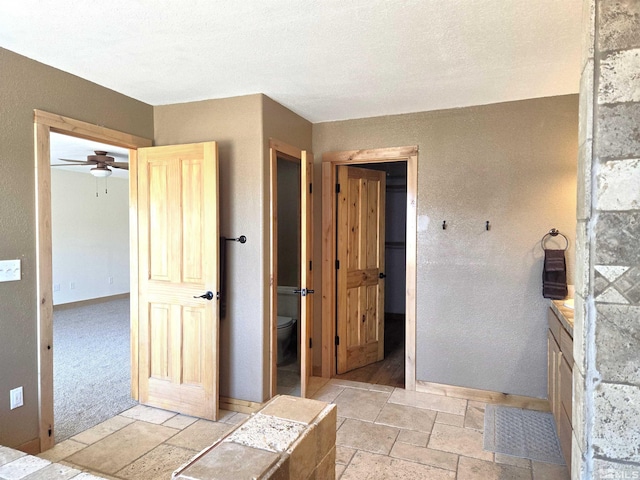 bathroom featuring toilet, a textured ceiling, stone tile flooring, baseboards, and vanity