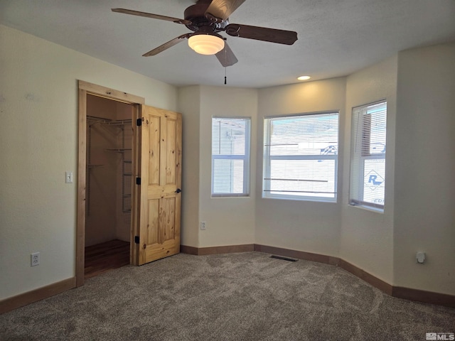 unfurnished bedroom featuring visible vents, a walk in closet, carpet floors, baseboards, and ceiling fan