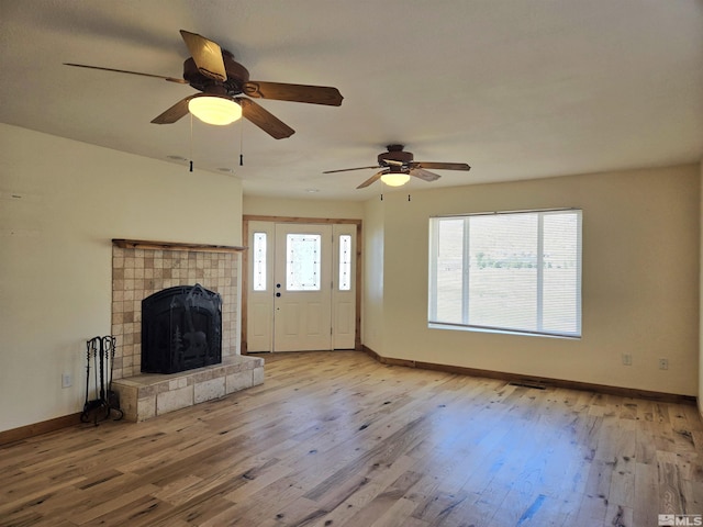 unfurnished living room with a tiled fireplace, wood finished floors, baseboards, and ceiling fan