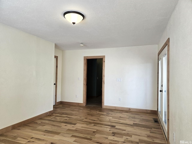 empty room featuring visible vents, a textured ceiling, light wood-type flooring, and baseboards