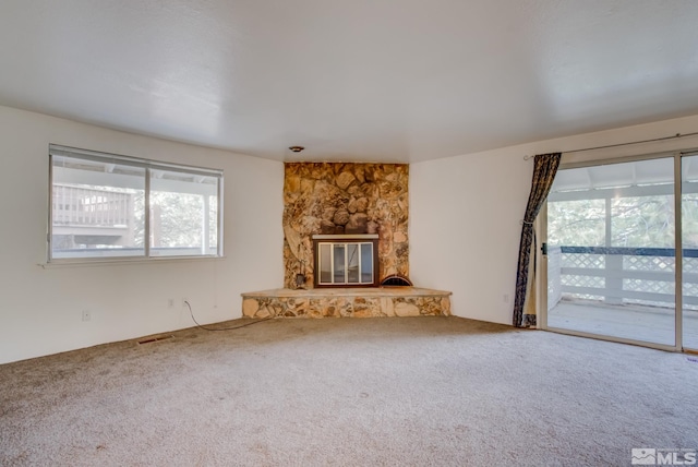 unfurnished living room with a stone fireplace and carpet flooring