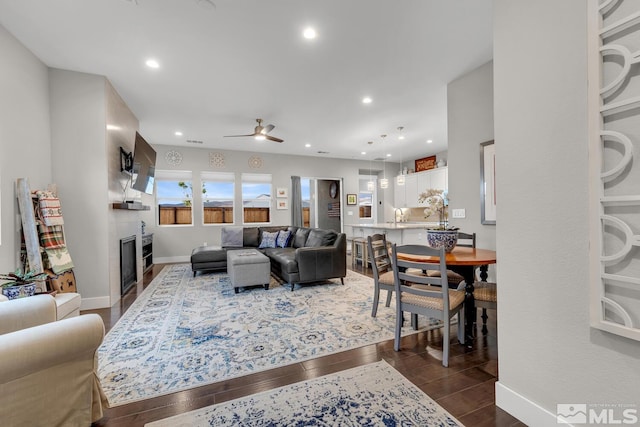 living room featuring ceiling fan, sink, a fireplace, and dark wood-type flooring