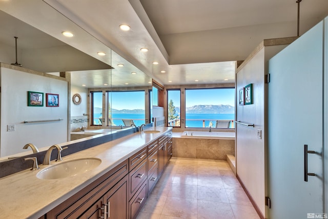 bathroom with a water and mountain view, tile patterned flooring, vanity, and a relaxing tiled tub