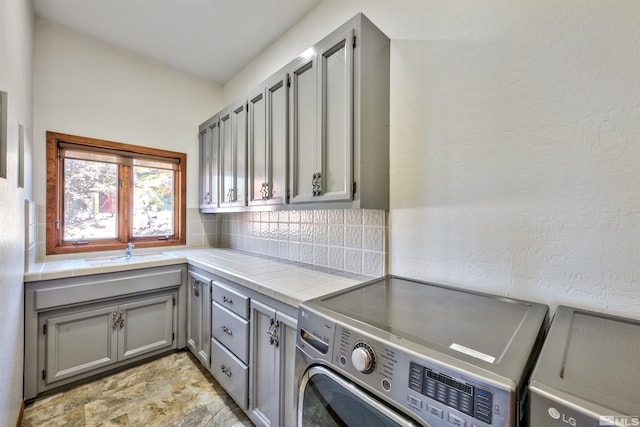 clothes washing area with washer and clothes dryer, cabinets, and sink