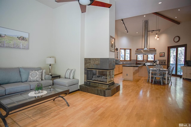 living room with ceiling fan, beam ceiling, high vaulted ceiling, light hardwood / wood-style floors, and a tiled fireplace