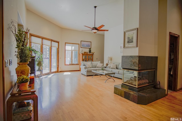 living room featuring a fireplace, ceiling fan, hardwood / wood-style floors, and a towering ceiling