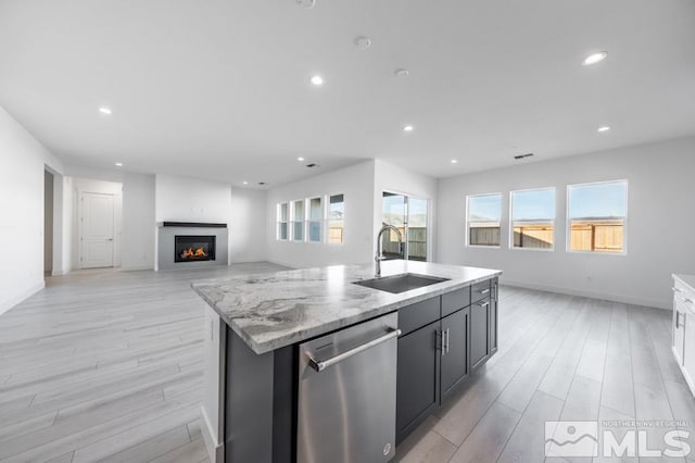 kitchen with sink, light hardwood / wood-style flooring, stainless steel dishwasher, an island with sink, and light stone counters