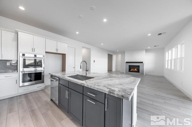 kitchen with light stone countertops, stainless steel appliances, sink, a center island with sink, and white cabinets