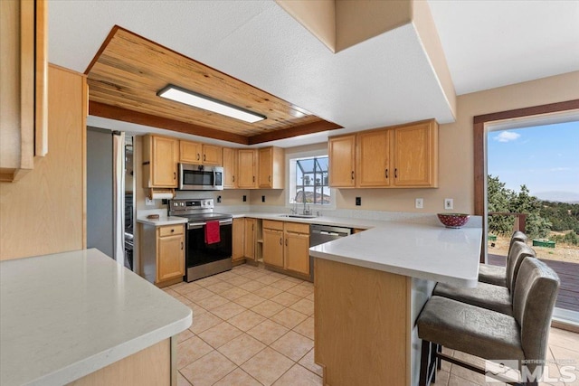 kitchen with light tile patterned flooring, sink, kitchen peninsula, appliances with stainless steel finishes, and a breakfast bar