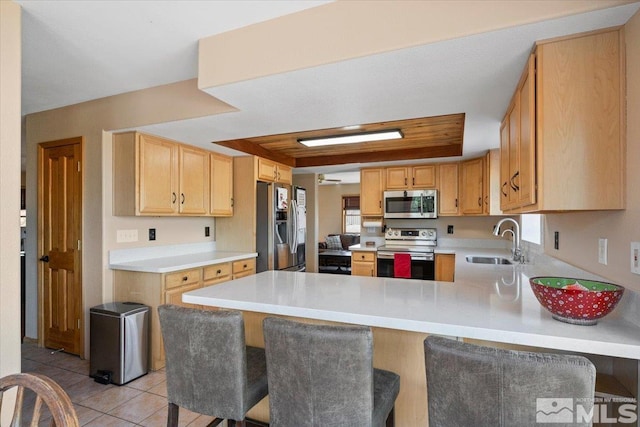 kitchen with light tile patterned floors, sink, kitchen peninsula, appliances with stainless steel finishes, and a kitchen breakfast bar