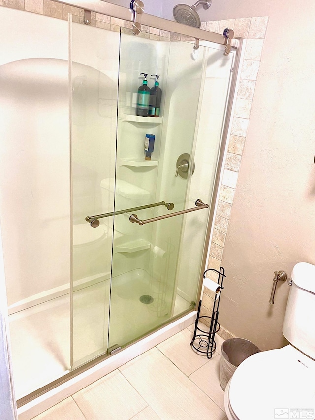 bathroom featuring a shower with door, toilet, and tile patterned floors