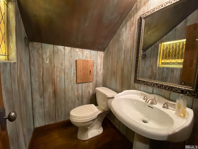 bathroom featuring sink, vaulted ceiling, wooden walls, hardwood / wood-style floors, and toilet