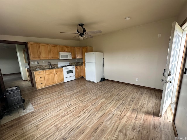 kitchen featuring light hardwood / wood-style floors, white appliances, a wood stove, ceiling fan, and sink