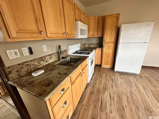 kitchen with light wood-type flooring, dark stone counters, white appliances, and sink