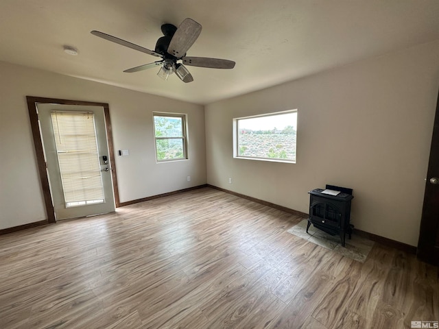 empty room with ceiling fan, light wood-type flooring, and a wood stove